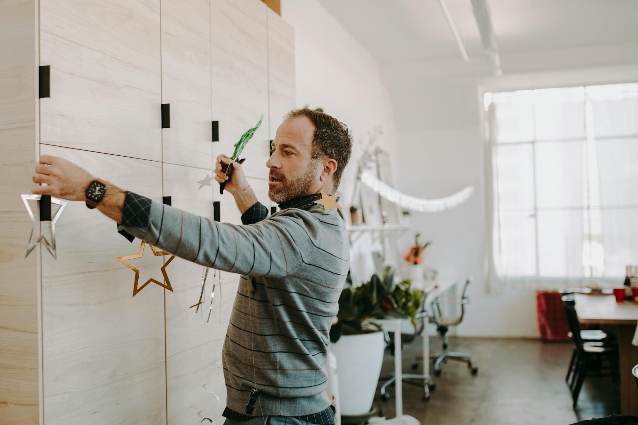 Man preparing decorations for a festive office holiday party. Cozy indoor setting.